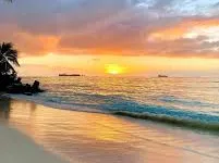 Tropical beach at sunset with orange sky reflecting on calm ocean waves