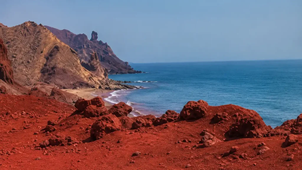 Red volcanic shoreline at Hormuz Red Beach in Iran with crimson sand meeting the Persian Gulf