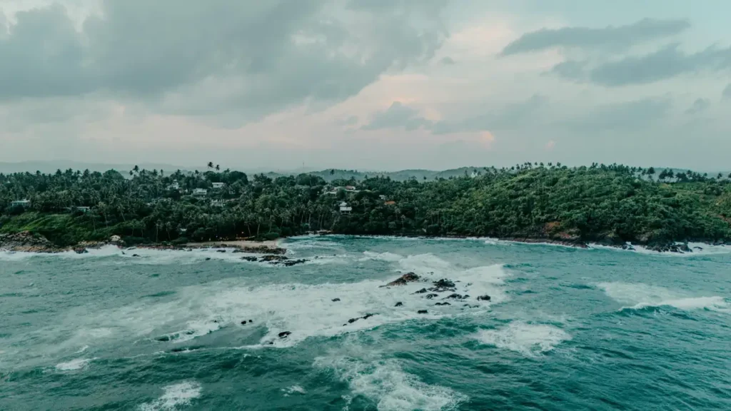 Blue Beach Hiriketiya aerial view with turquoise waves, rocky reef, and tropical coastline in Sri Lanka