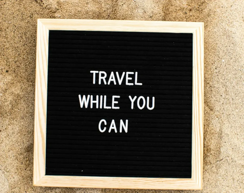Travel tips sign on sandy beach reading “travel while you can” near Hiriketiya Sri Lanka 