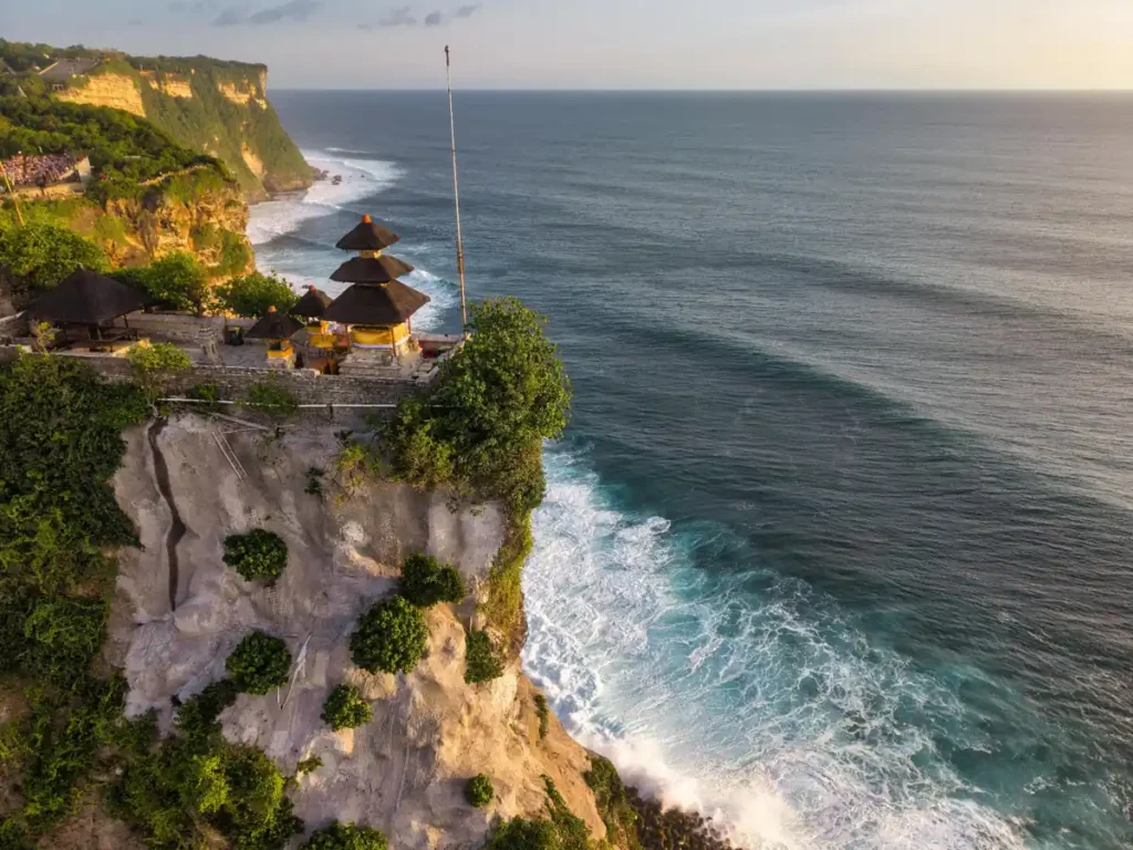 Golden sunset over Bali cliffs and ocean waves viewed from above.