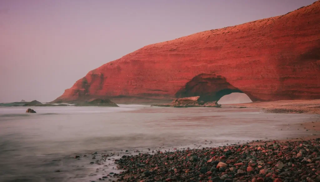 Red rocky cliffs and calm shoreline at Hormuz Red Beach during sunset on Hormuz Island, Iran.
