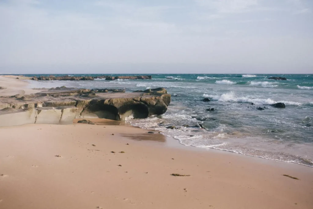 Rocky shoreline and soft sandy coast at Qeshm Island Beach with turquoise waves under a clear sky in Iran.
