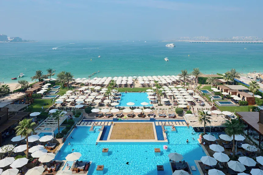 Aerial view of Rixos Premium Dubai JBR featuring luxury pools, private beachfront access, palm trees, and turquoise Arabian Gulf waters.