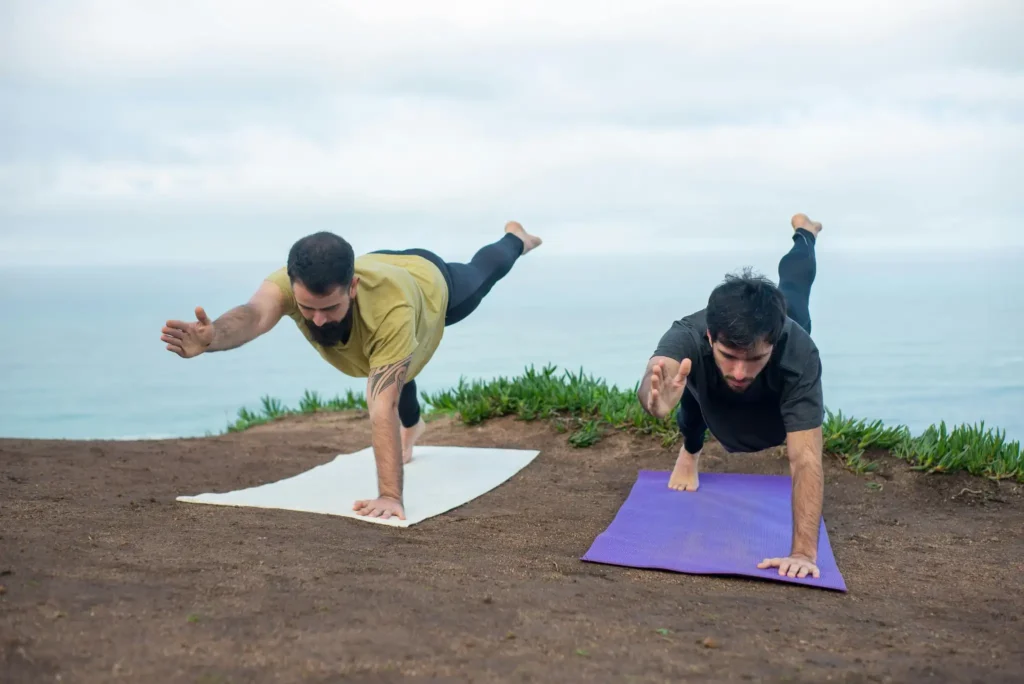 Two travellers practicing yoga poses on cliffside mats overlooking the Arabian Sea near Agonda Beach in South Goa.