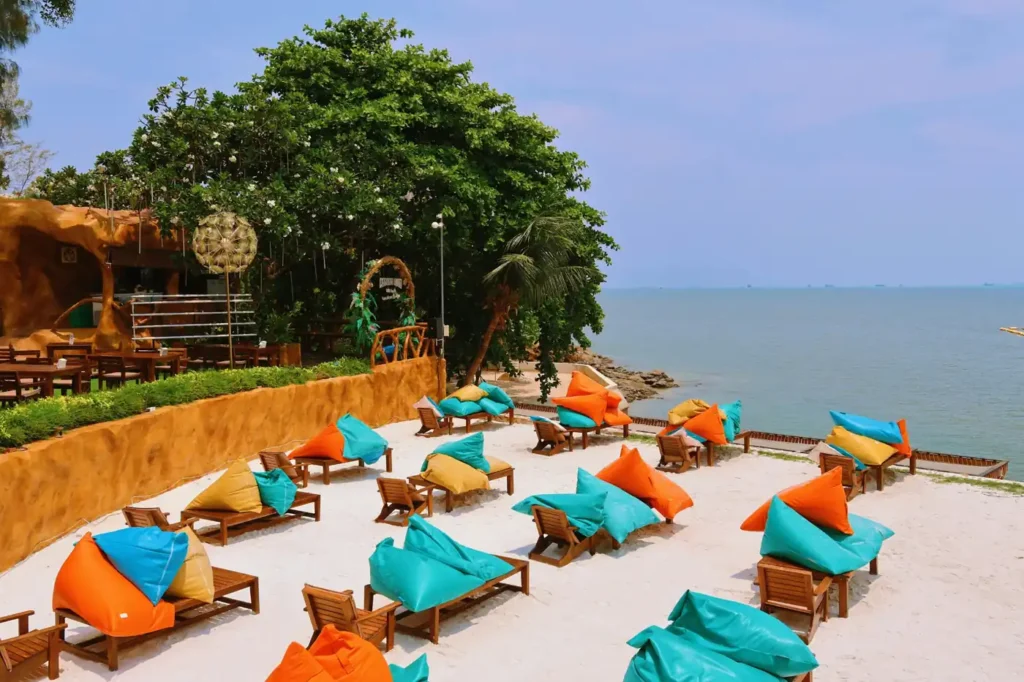 Colorful bean bag lounge chairs on a sandy beachfront terrace overlooking the ocean at a tropical beach resort in Thailand.