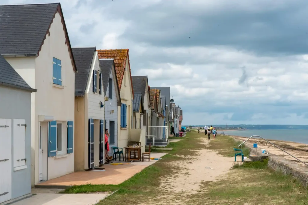 Row of beachfront coastal houses beside a sandy shoreline with cloudy skies, peaceful seaside path, and calm ocean views near the beach village coast