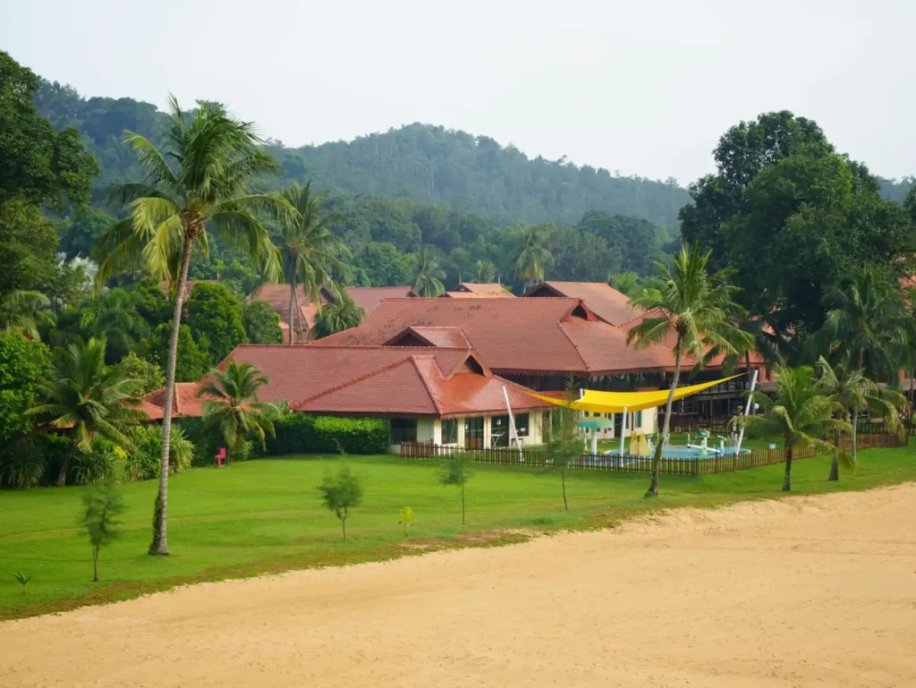 Beachfront tropical resort in Palawan surrounded by palm trees, green hills, and sandy shoreline under a calm tropical sky.