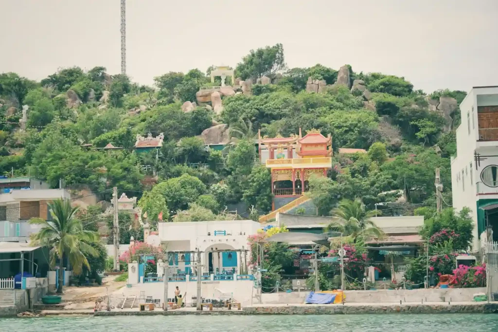 Colorful waterfront village and hillside temple surrounded by lush greenery on Binh Ba Island in Vietnam.