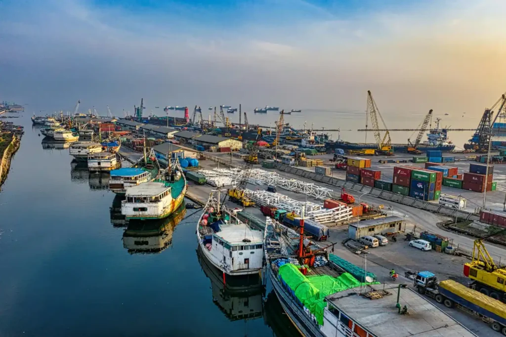 Aerial view of Chabahar Port in Iran with cargo ships, fishing boats, and industrial docks along the Gulf of Oman coastline.