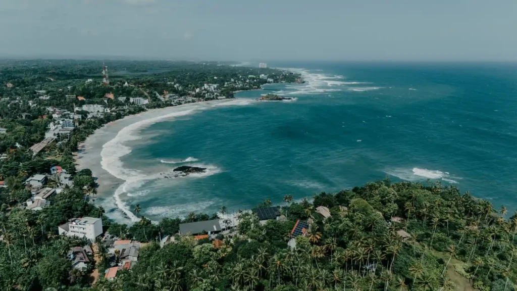 Aerial view of a tropical coastline with turquoise sea and palm trees.