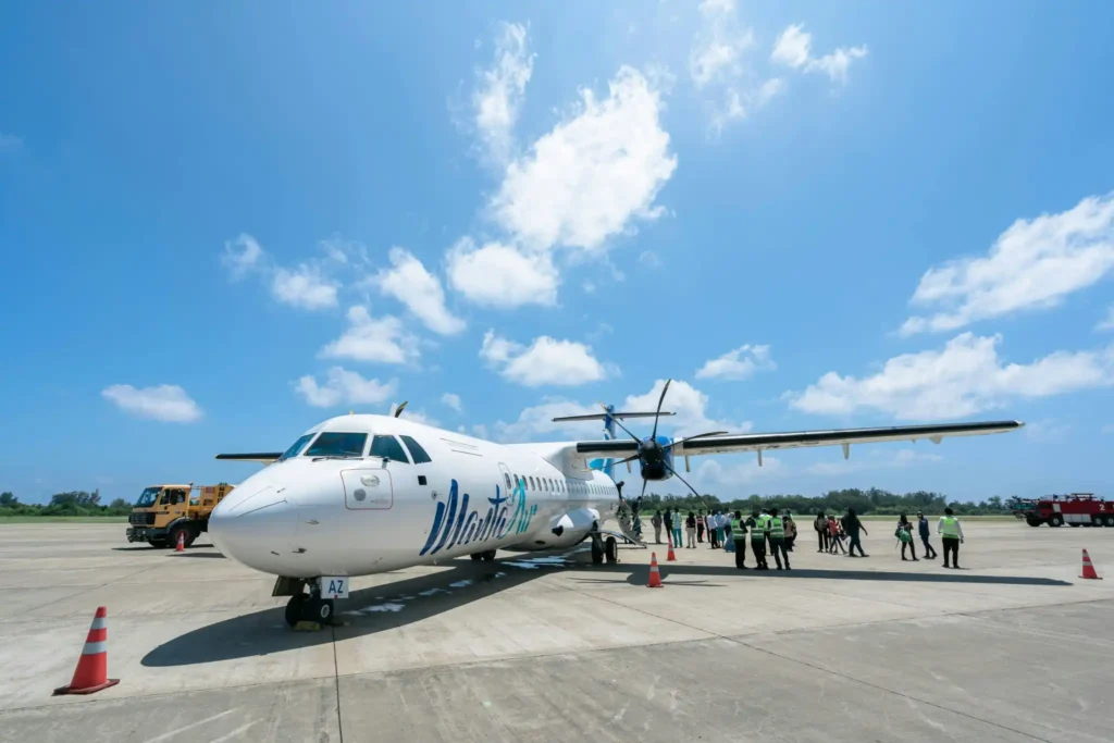 Passenger turboprop airplane parked at Con Dao Airport with travelers boarding on a sunny day in Vietnam.