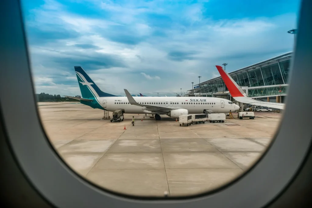 View of a SilkAir airplane parked at the airport runway seen through an airplane window under cloudy skies in Vietnam