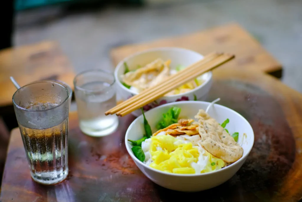 Traditional Vietnamese noodle bowls with fresh vegetables and chopsticks served on a wooden table in Con Dao