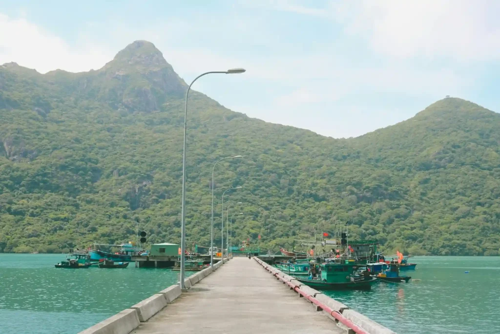 Fishing boats docked beside a long pier with green mountains and turquoise water in Con Dao Vietnam