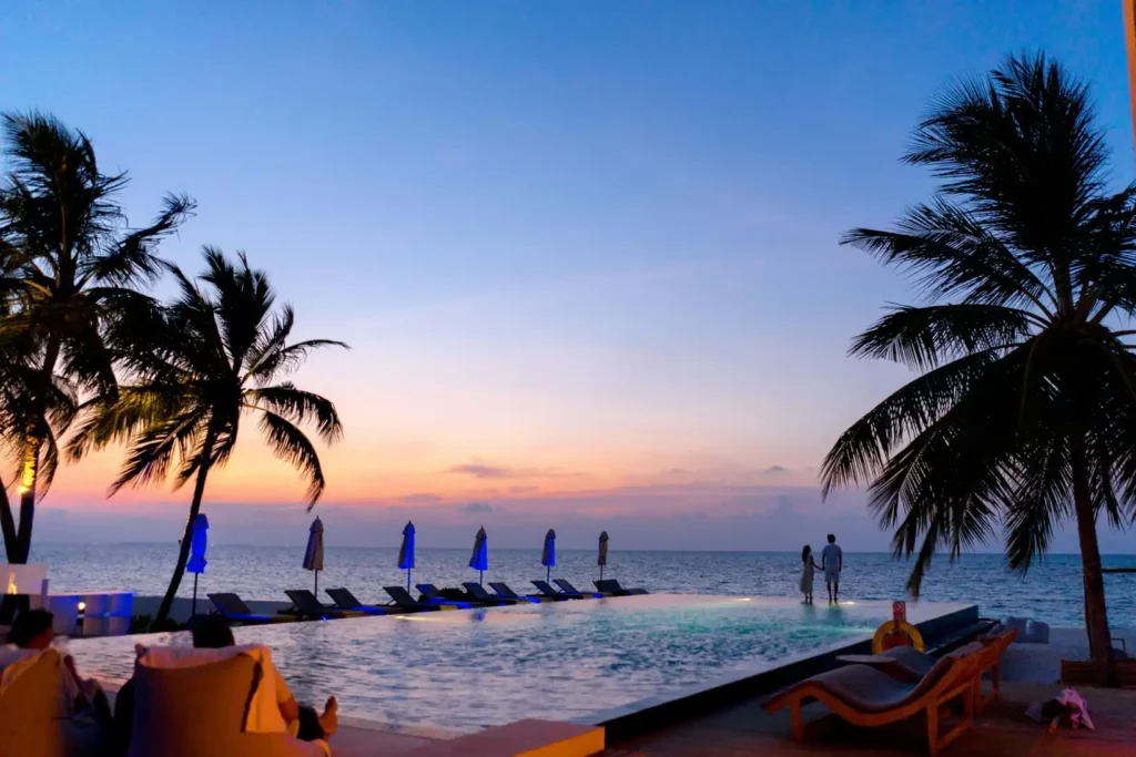 Luxury beachfront infinity pool resort in Con Dao at sunset with palm trees, ocean views, and couples relaxing by the sea.
