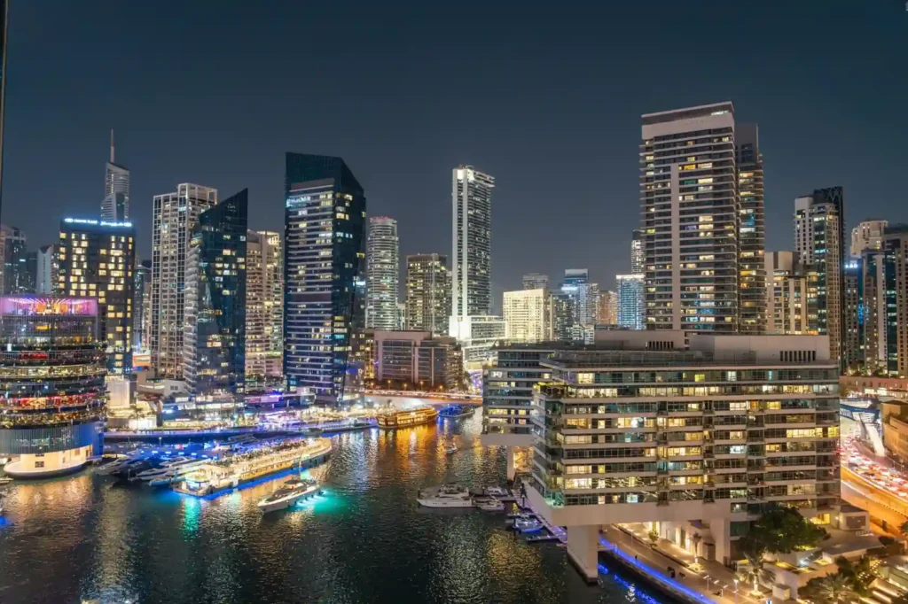 Dubai Marina skyline at night with illuminated skyscrapers, luxury yachts, and colorful waterfront reflections along the canal.