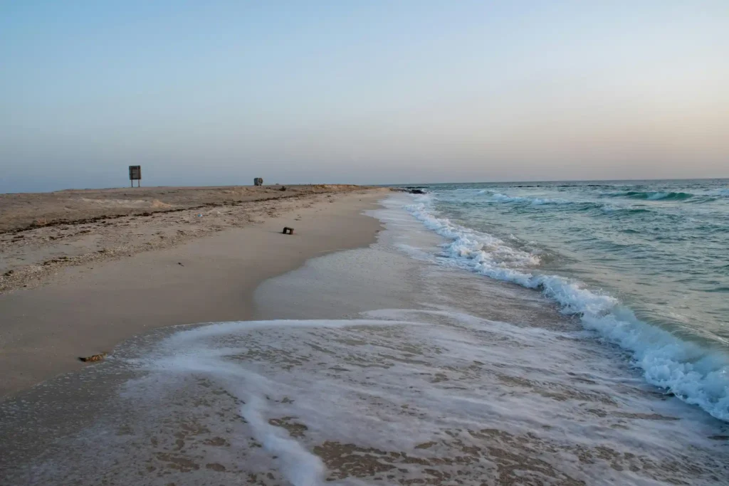 Gentle waves washing onto the quiet sandy shoreline of Hengam Island Beach in Iran during sunset with calm Persian Gulf waters.