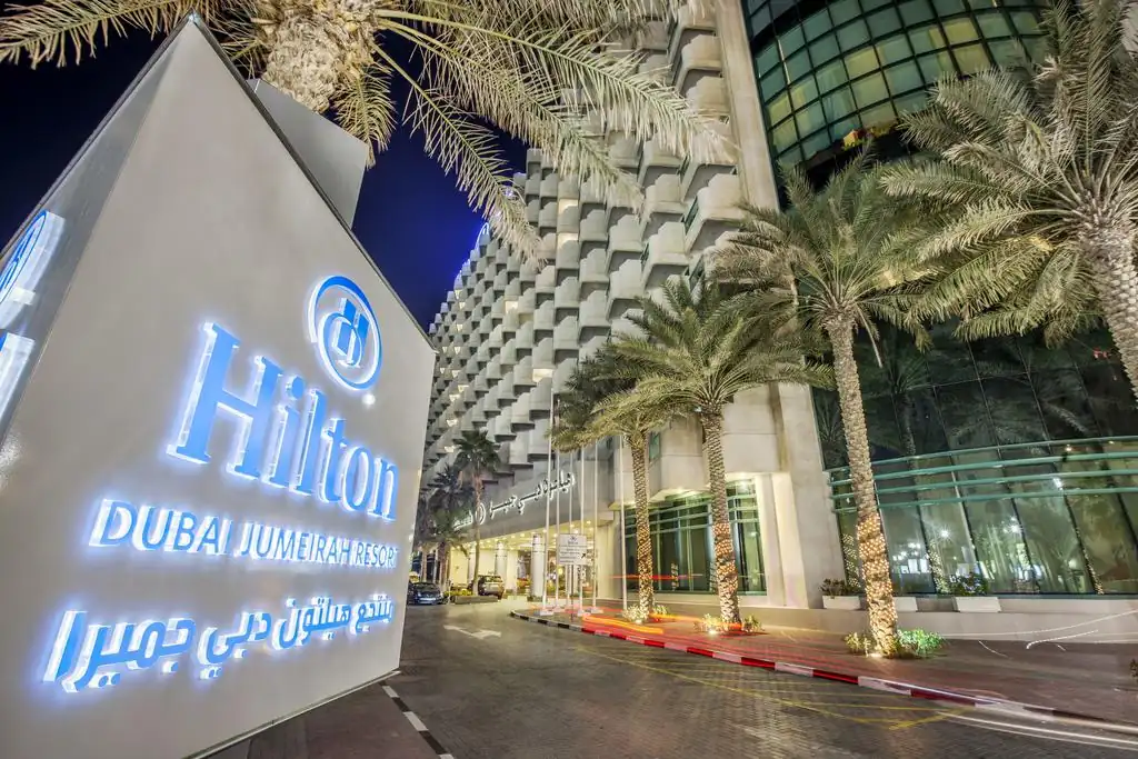 Night view of Hilton Dubai Jumeirah hotel entrance with illuminated signage, palm trees, and modern luxury architecture near JBR Beach in Dubai.