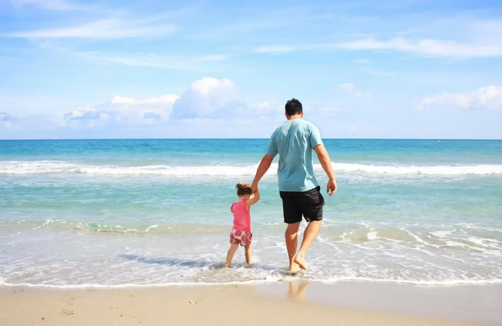 Father holding a child’s hand while walking into the ocean