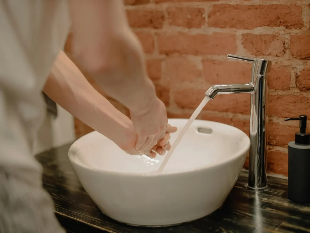 Person washing hands under running water in a sink, emphasizing hygiene 
