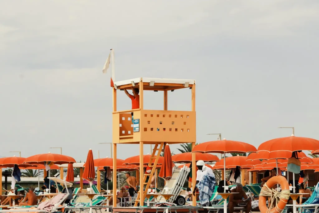 Lifeguard on a watchtower overlooking a busy beach with orange umbrellas and swimmers at Hiriketiya Beach