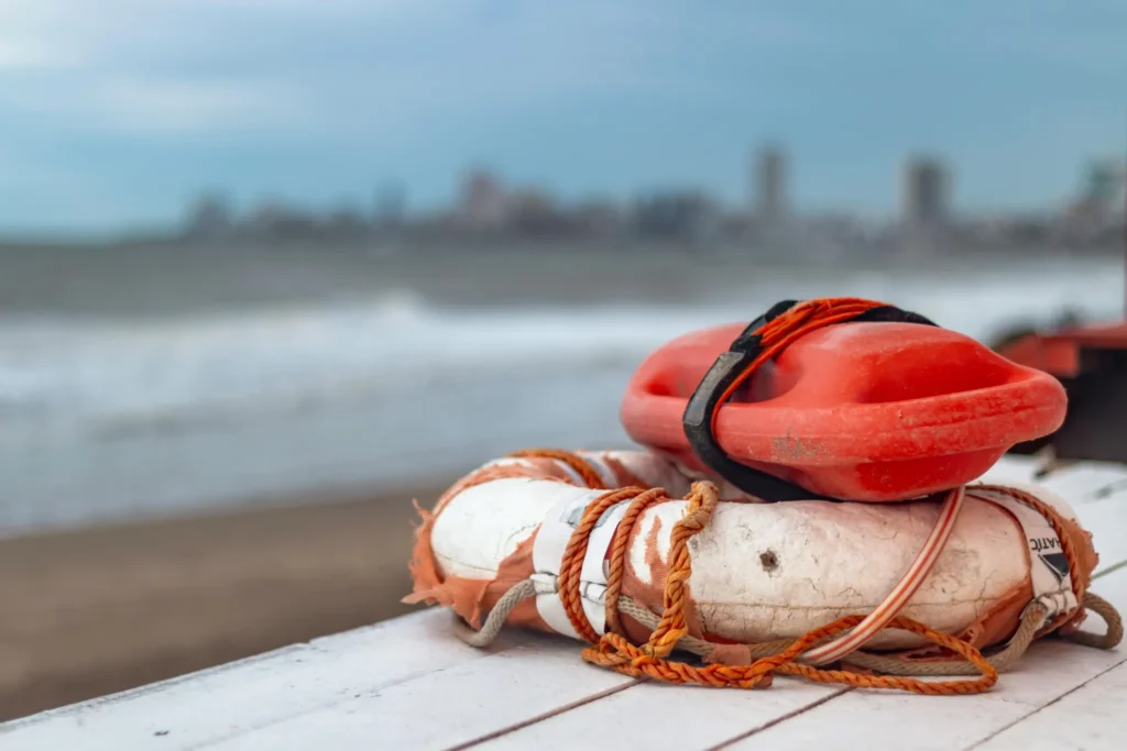 Lifesaving ring and flotation device on a beach with ocean waves and a blurred coastal city in the background
