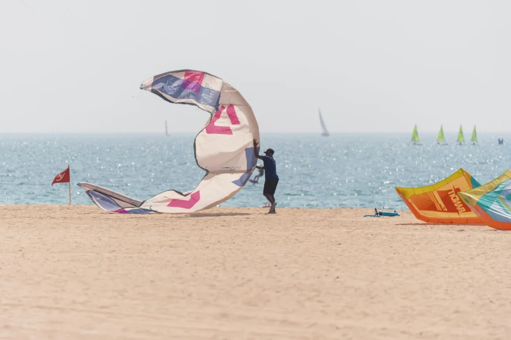 Kitesurfer preparing colorful kiteboarding equipment on the sandy shores of Kite Beach Dubai with the Arabian Gulf in the background.