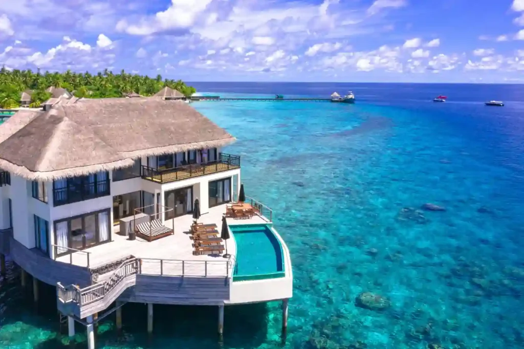 Luxury overwater villa resort with a private infinity pool above crystal-clear turquoise ocean water on a tropical island.