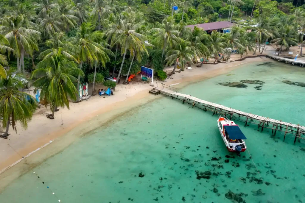 Aerial view of Nam Du Island in Vietnam featuring crystal-clear turquoise water, palm-lined beach, wooden pier, and a small boat anchored near the shore.