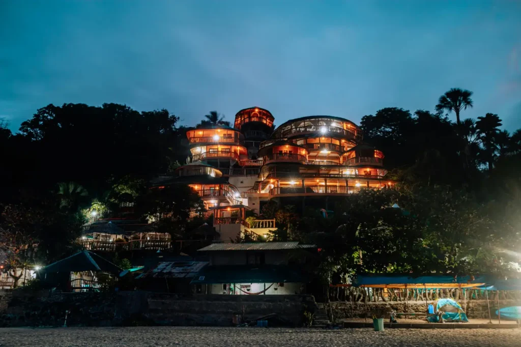 Luxury hillside beach resort glowing at night in Palawan, surrounded by tropical trees and overlooking a quiet sandy shoreline.