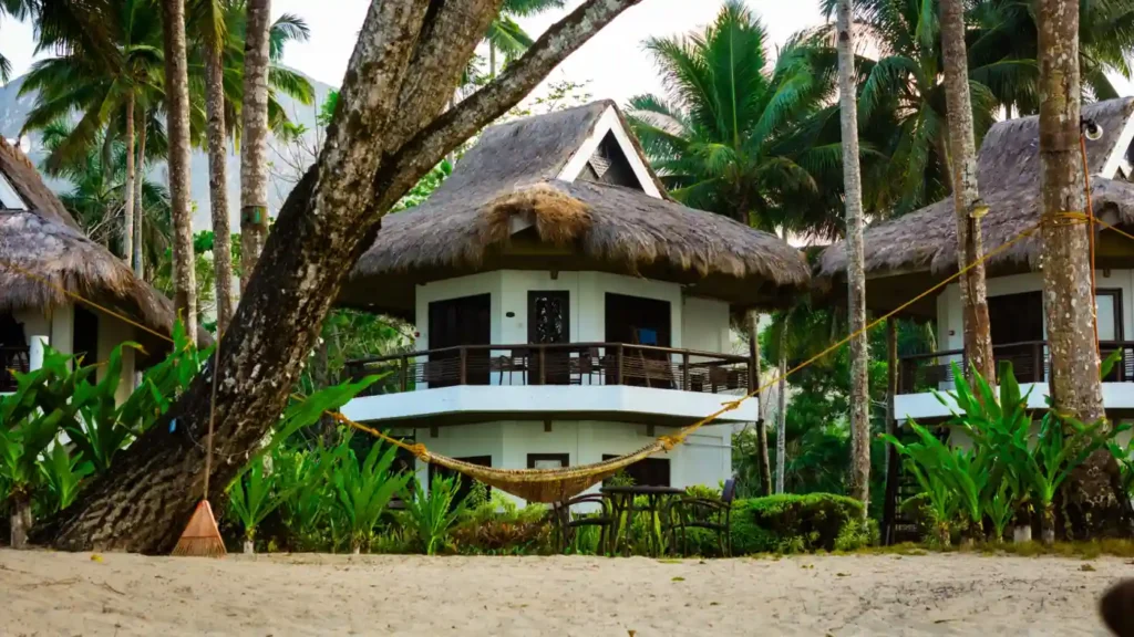 Beachfront tropical resort cottages surrounded by palm trees and hammocks near Port Barton in Palawan, Philippines.