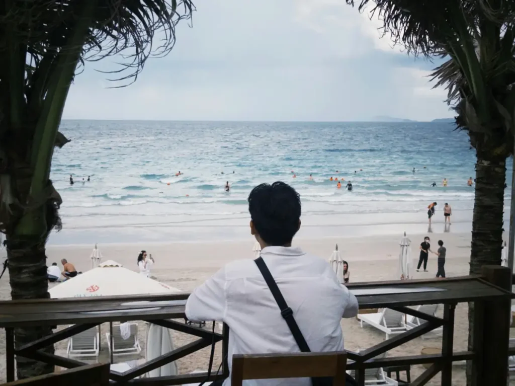 Traveler sitting at a beachfront café overlooking the ocean and swimmers at a tropical beach in Port Barton, Palawan.