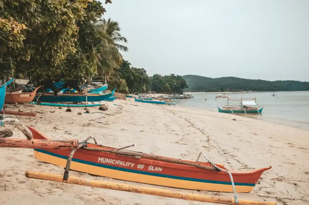 Traditional fishing boats resting along the sandy shoreline of Port Barton in Palawan surrounded by palm trees and calm coastal water.