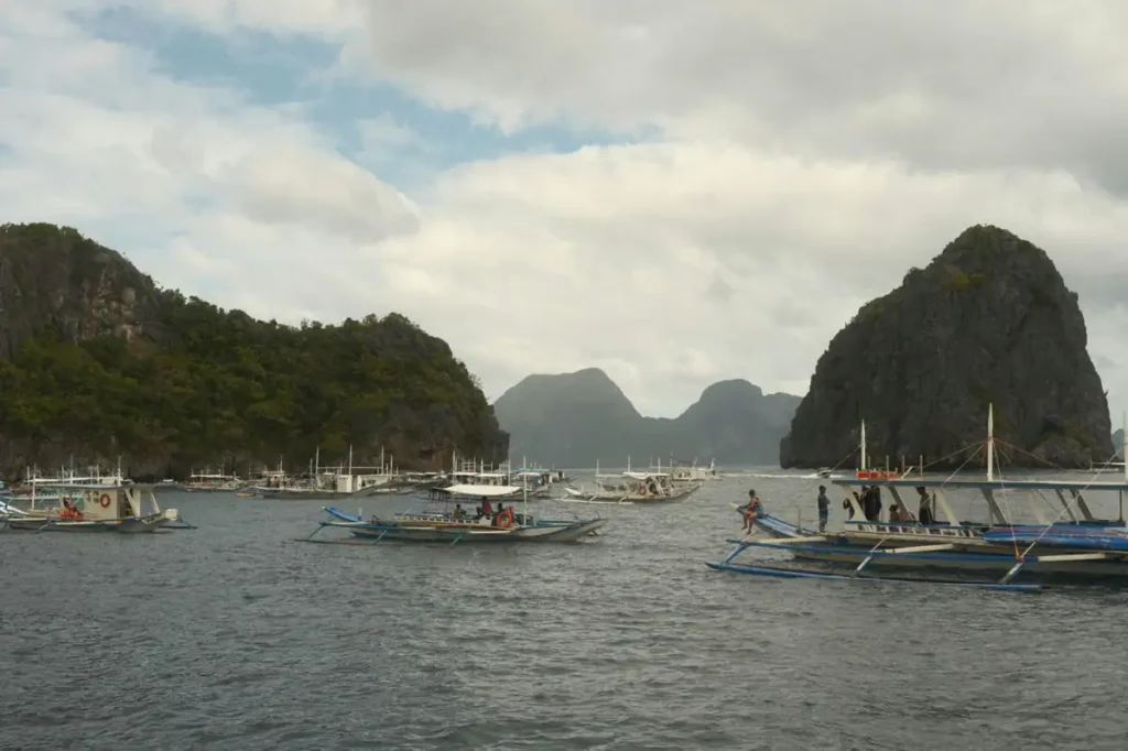 Traditional island hopping boats floating between limestone cliffs and tropical islands in the waters near Port Barton, Palawan.