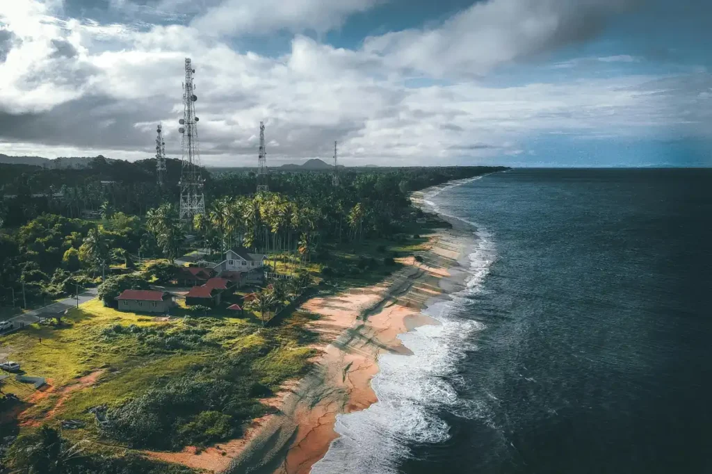 Aerial view of Port Barton coastline with mobile network towers, tropical palm trees, and beachfront houses along the Palawan shore.
