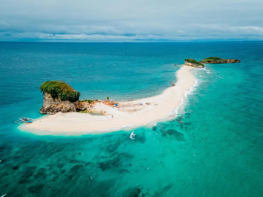 Aerial view of a white sandbar island in Port Barton surrounded by crystal-clear turquoise water and small rocky islets in Palawan.