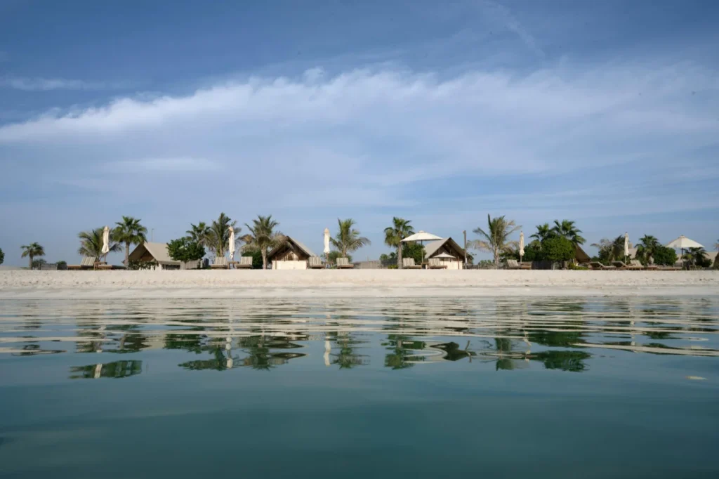 Scenic view of Saadiyat Public Beach Abu Dhabi with calm turquoise waters, beachfront villas, palm trees, and relaxing coastal atmosphere.