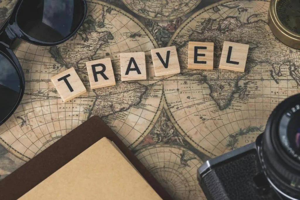 Vintage world map with travel accessories, camera, sunglasses, compass, and wooden letter tiles spelling travel concept for tourism planning