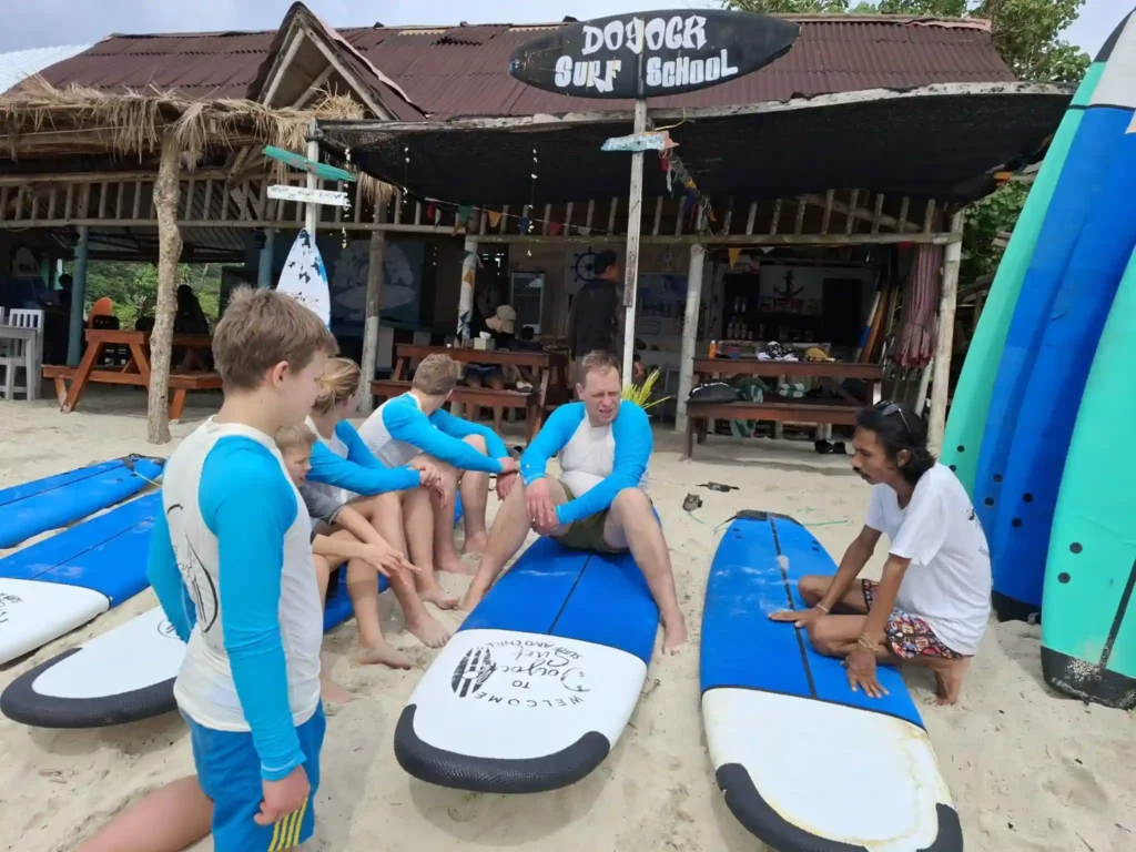 Surf instructor giving a beach lesson to a group of beginner surfers beside blue surfboards at a surf school on Selong Belanak Beach, Lombok, Indonesia