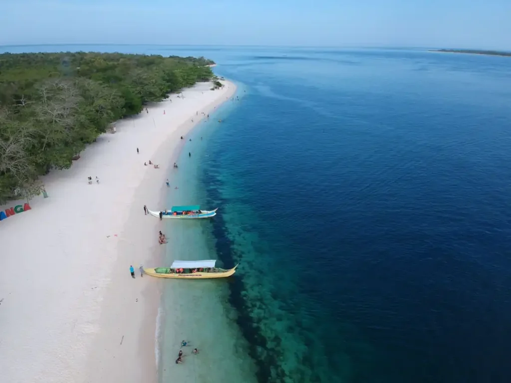 Aerial view of a white-sand beach with boats anchored beside crystal-clear turquoise water.