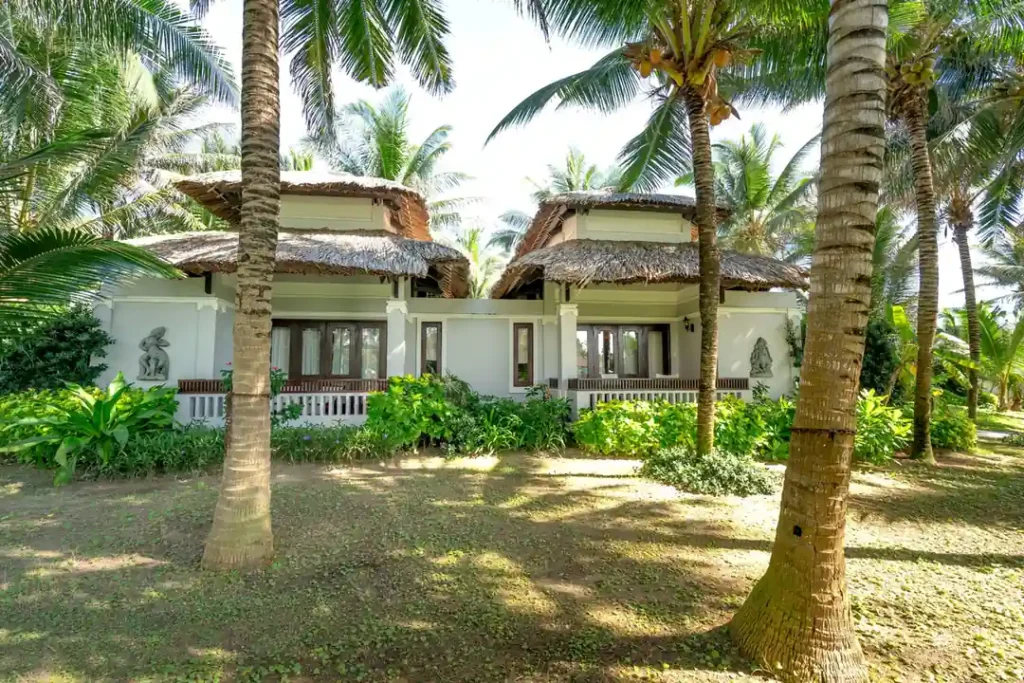 Tropical resort villas in Bohol surrounded by coconut palm trees, thatched roofs, and lush green garden scenery.