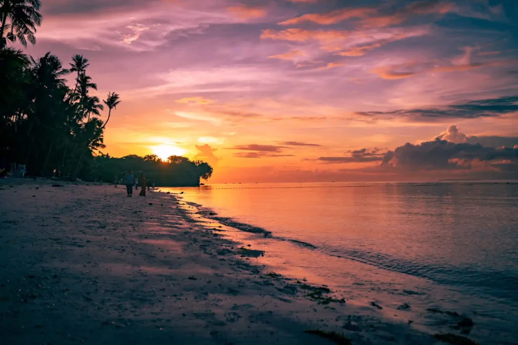 Sunset at Anda Beach in Bohol, Philippines, with colorful pink and orange skies reflecting on calm ocean waters along a tropical palm-lined shoreline.