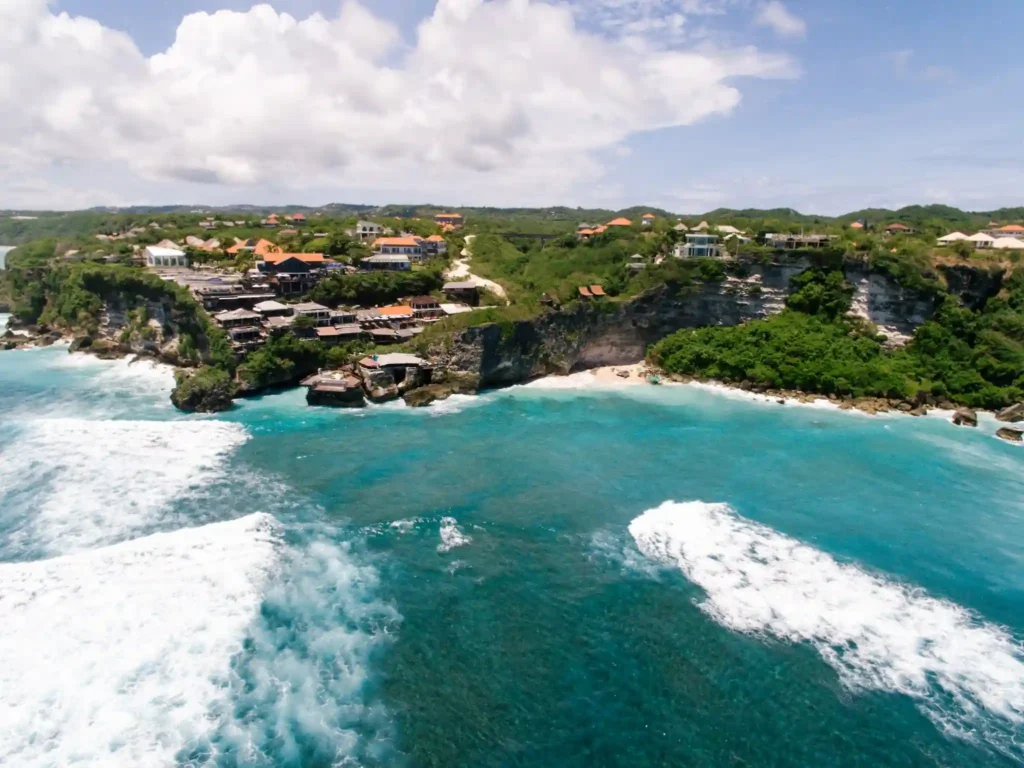 Aerial view of Balangan Beach coastline with turquoise water, waves, and cliffside resorts in Bali.
