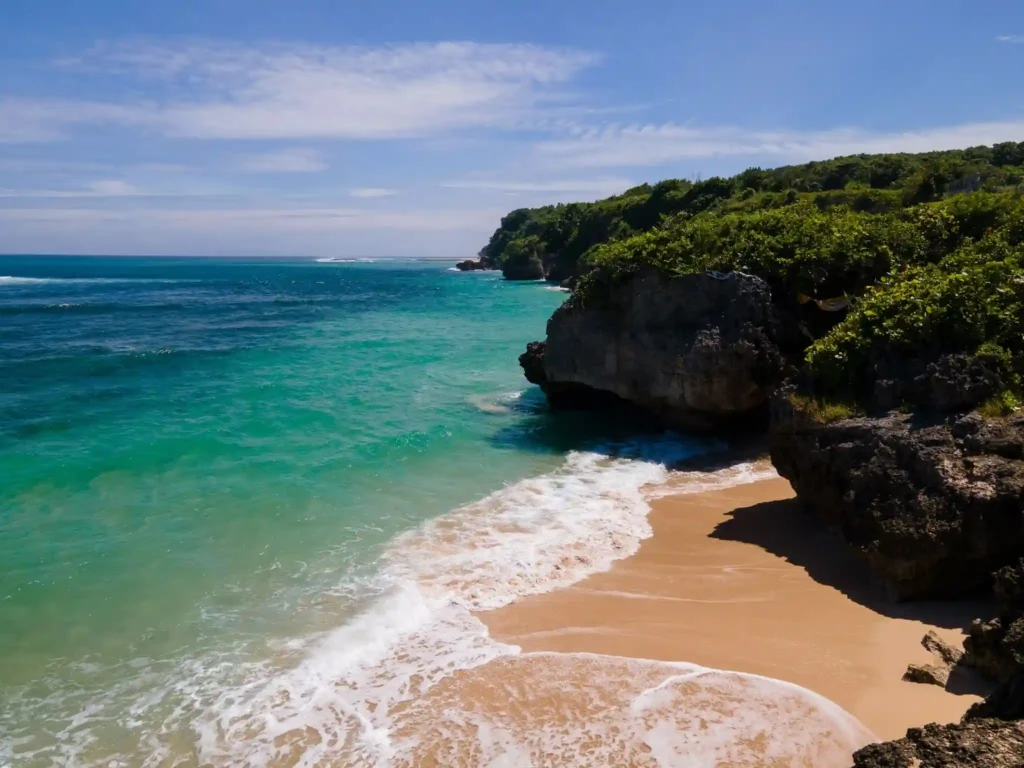 Balangan Beach in Bali featuring turquoise ocean water, golden sand, and dramatic limestone cliffs along the tropical coastline.