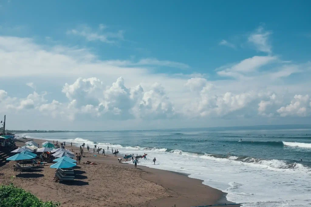 Surfers and beachgoers at Balangan Beach Bali enjoying ocean waves, sandy shoreline, and beach umbrellas under a bright blue sky.