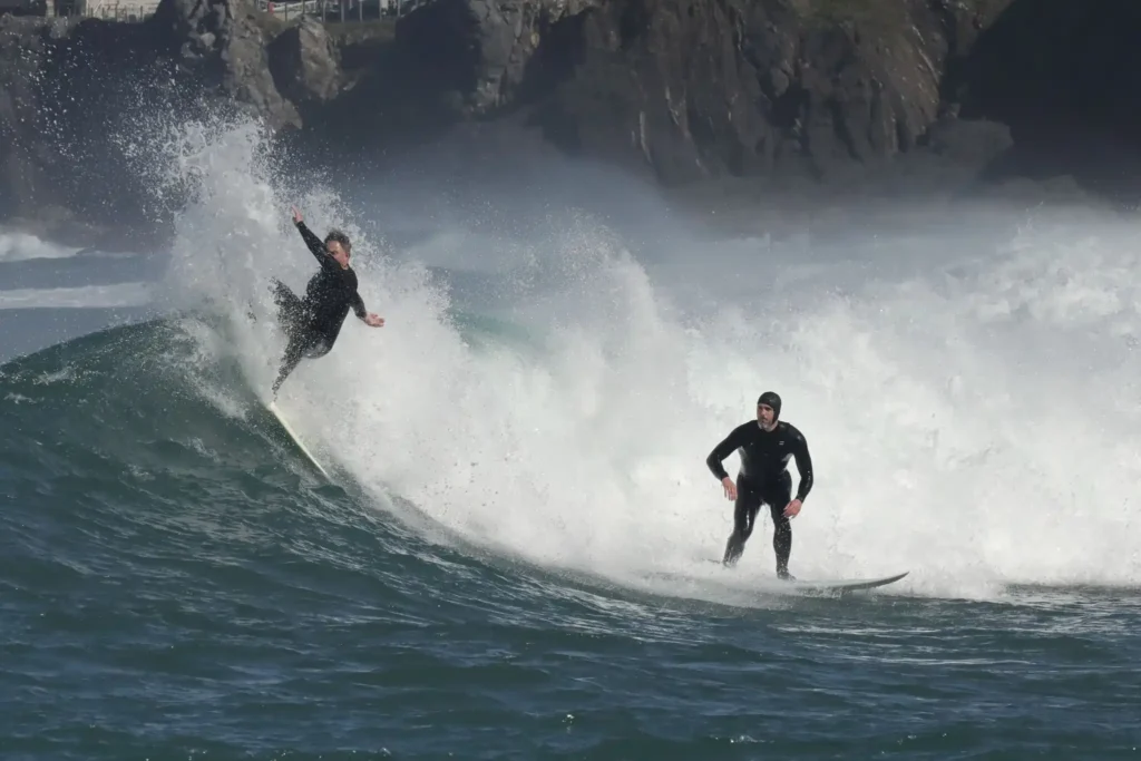 Surfers riding powerful ocean waves at Balangan Beach Bali, with whitewater spray and dramatic coastal cliffs in the background.