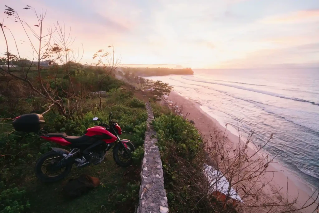 Motorcycle parked at a cliffside viewpoint overlooking Balangan Beach in Bali during sunset, with sweeping coastal views and gentle ocean waves.