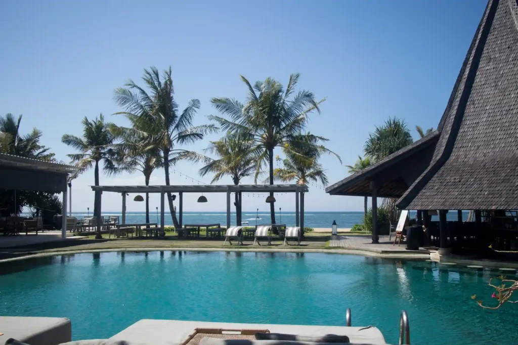 Beachfront resort pool with palm trees overlooking the ocean in Bali. 