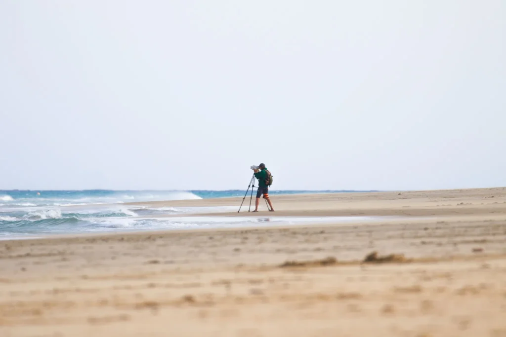 Photographer capturing coastal landscape on a quiet sandy beach with ocean waves and clear horizon